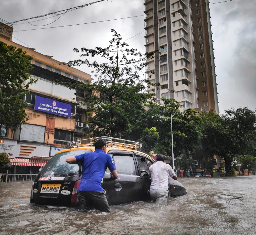 men pushing car through city floodwaters